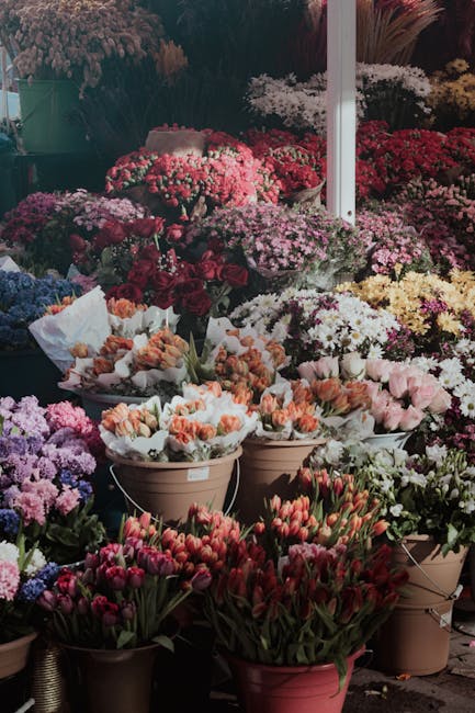 A vibrant display of flower arrangements at a florist shop, featuring a variety of fresh flowers including tulips in shades of red, pink, and orange, along with clusters of small pink, purple, and whi