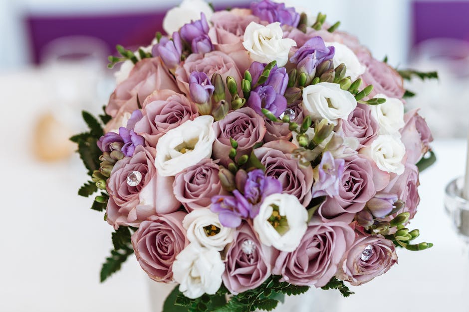 A close-up view of a floral arrangement consisting of soft pink roses, white eustoma, and purple freesias, arranged in a rounded bouquet style. The flowers are fresh with delicate, slightly waxy petal